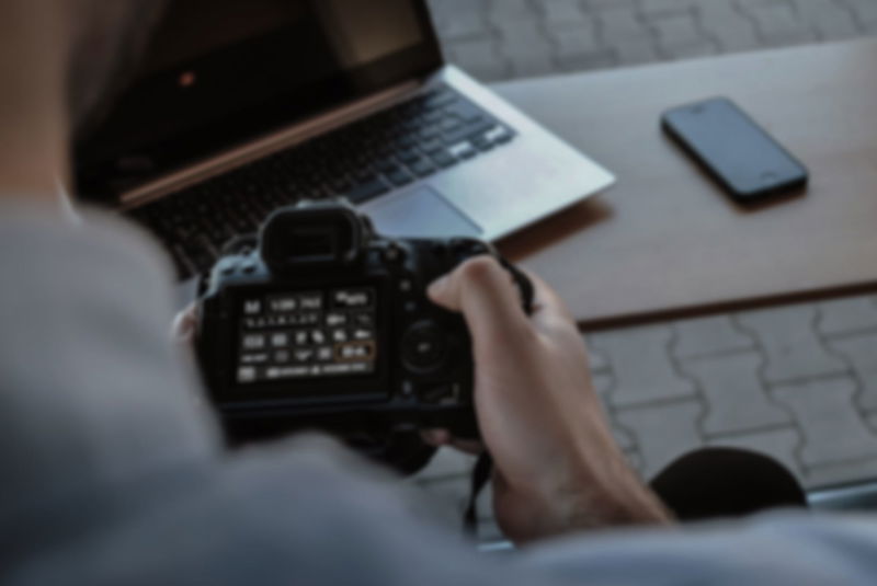 photographer operating a camera with laptop and phone lying on a table in front of him